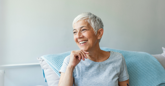 A contented retirement-age woman relaxes on her sofa and smiles confidently.